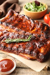 Photo of Tasty roasted pork ribs served with rosemary, sauce and salad on wooden table, closeup