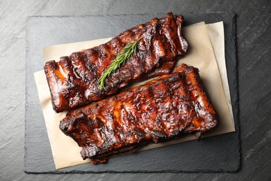 Photo of Tasty roasted pork ribs served with rosemary on black table, top view
