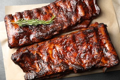 Photo of Tasty roasted pork ribs served with rosemary on black table, top view