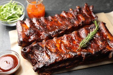 Photo of Tasty roasted pork ribs served with rosemary, sauce and salad on black table, closeup
