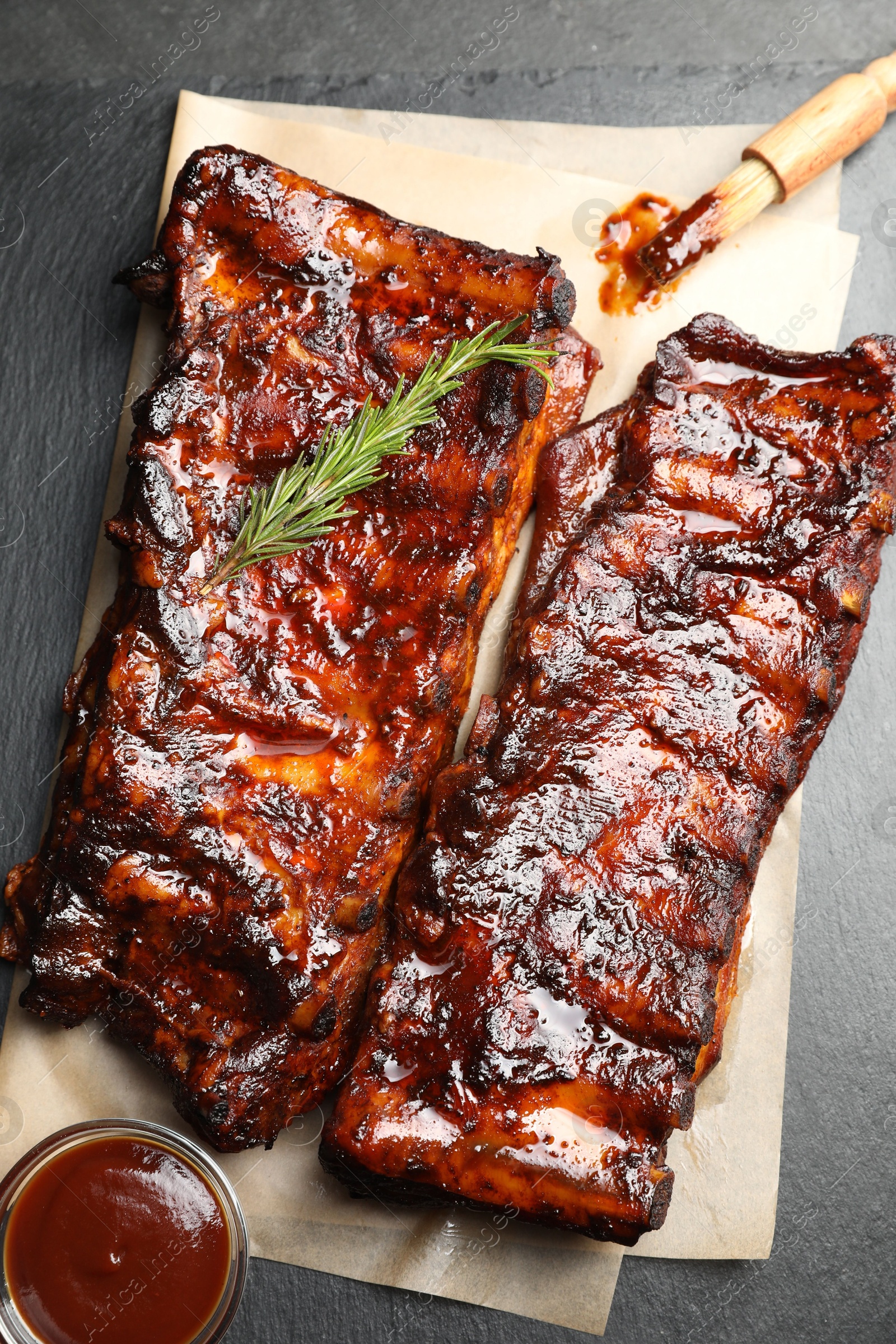 Tasty roasted pork ribs served with rosemary and sauce on black table, top view Photo of Tasty roasted pork ribs served with rosemary and sauce on black table, top view