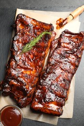 Photo of Tasty roasted pork ribs served with rosemary and sauce on black table, top view
