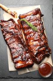 Photo of Tasty roasted pork ribs served with rosemary and sauce on black table, top view