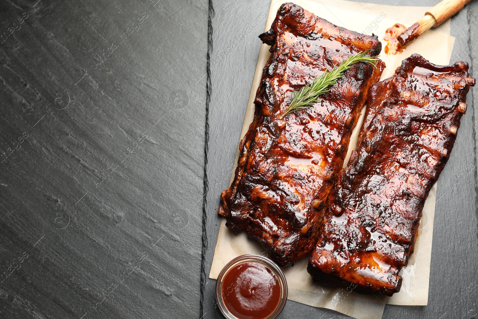 Tasty roasted pork ribs served with rosemary and sauce on black table, top view. Space for text Photo of Tasty roasted pork ribs served with rosemary and sauce on black table, top view. Space for text
