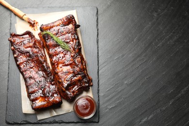 Photo of Tasty roasted pork ribs served with rosemary and sauce on black table, top view. Space for text