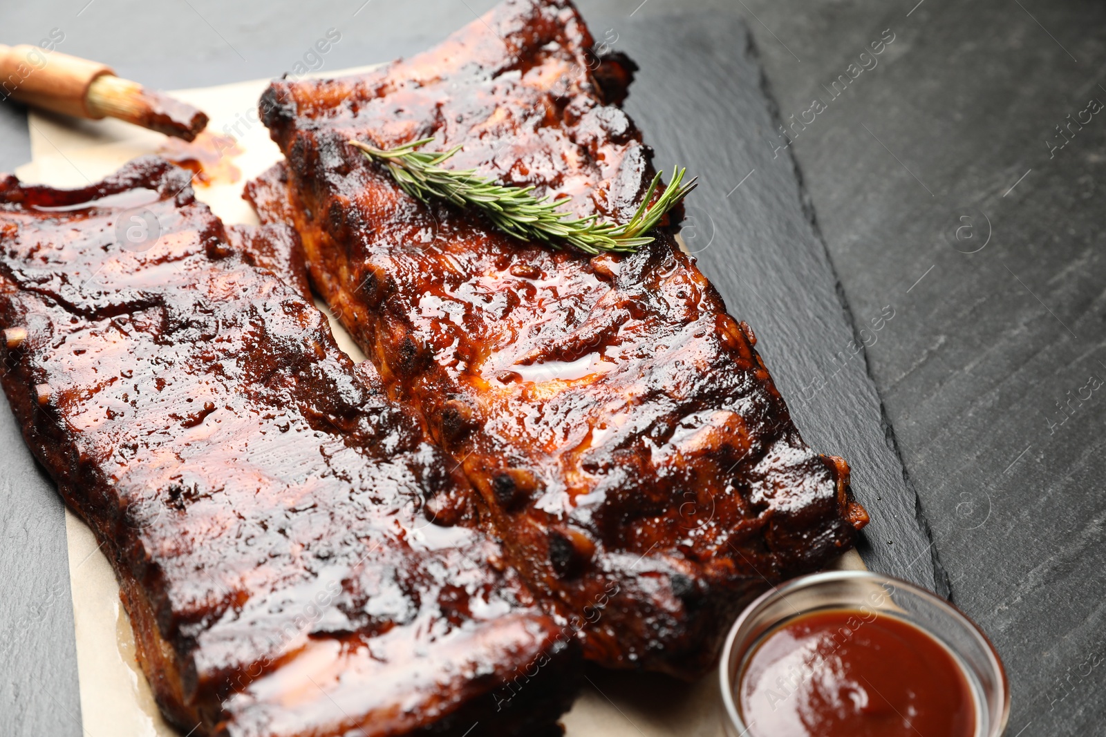Tasty roasted pork ribs served with rosemary and sauce on black table, closeup Photo of Tasty roasted pork ribs served with rosemary and sauce on black table, closeup