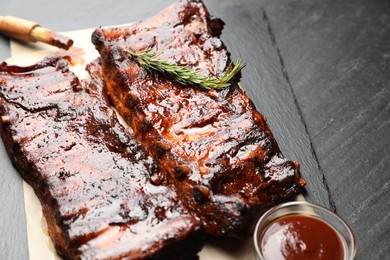 Photo of Tasty roasted pork ribs served with rosemary and sauce on black table, closeup