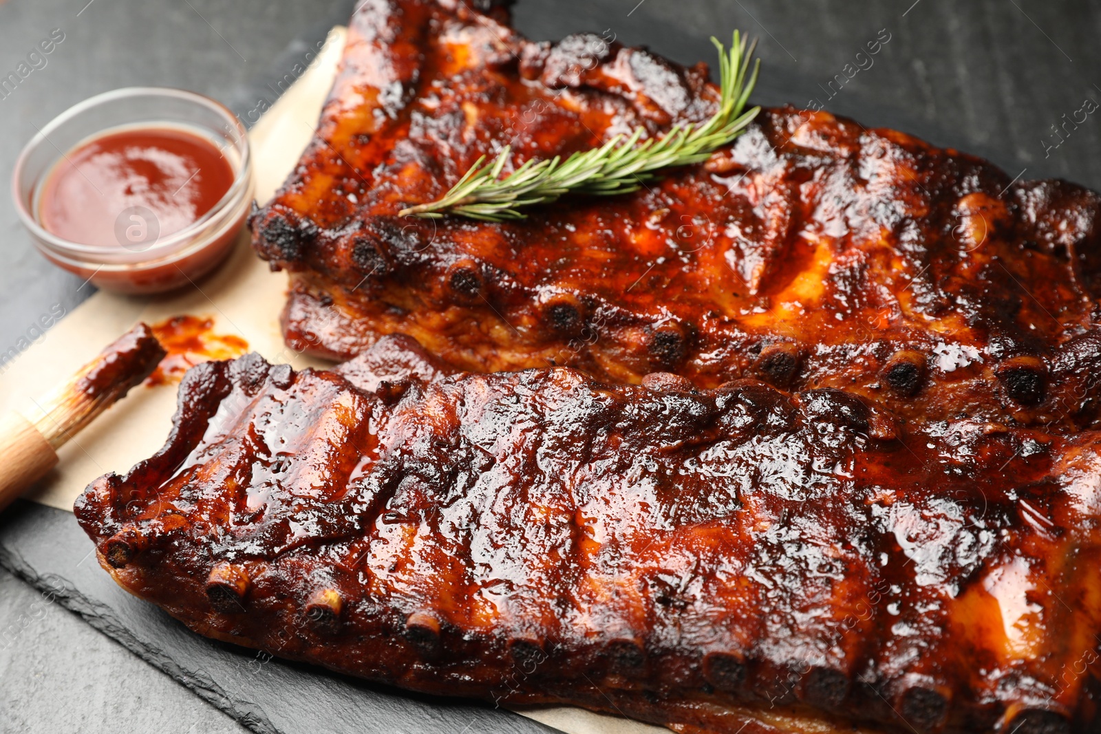 Tasty roasted pork ribs served with rosemary and sauce on black table, closeup Photo of Tasty roasted pork ribs served with rosemary and sauce on black table, closeup