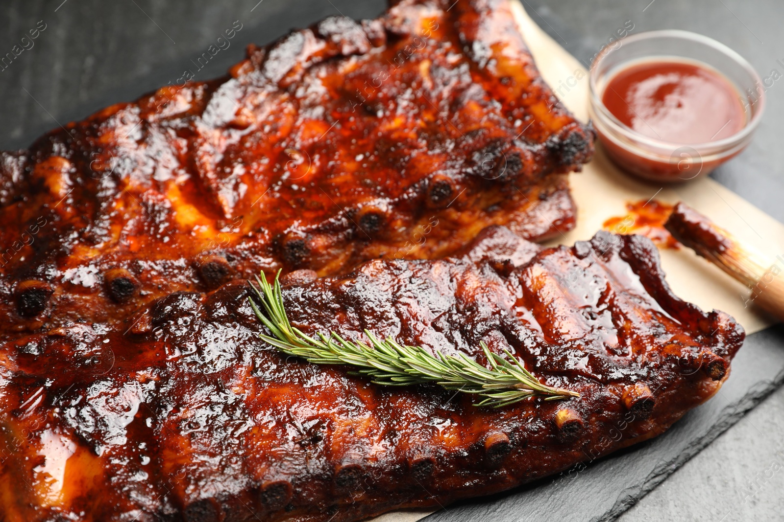 Tasty roasted pork ribs served with rosemary and sauce on black table, closeup Photo of Tasty roasted pork ribs served with rosemary and sauce on black table, closeup