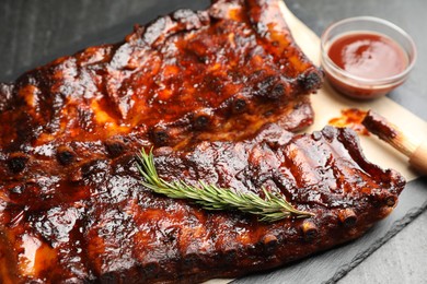Photo of Tasty roasted pork ribs served with rosemary and sauce on black table, closeup