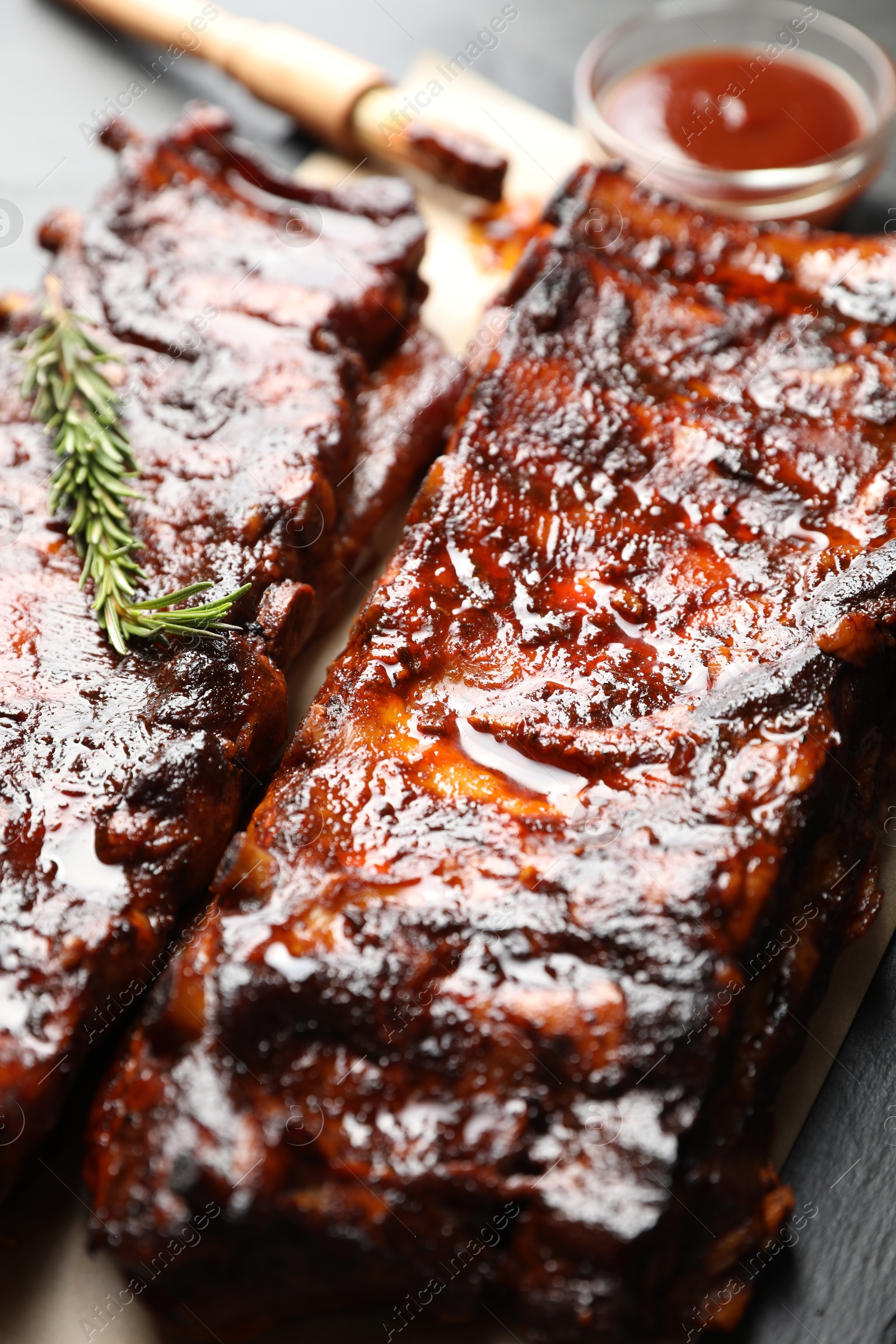 Tasty roasted pork ribs served with rosemary and sauce on black table, closeup Photo of Tasty roasted pork ribs served with rosemary and sauce on black table, closeup