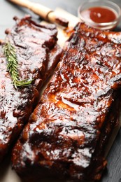 Photo of Tasty roasted pork ribs served with rosemary and sauce on black table, closeup