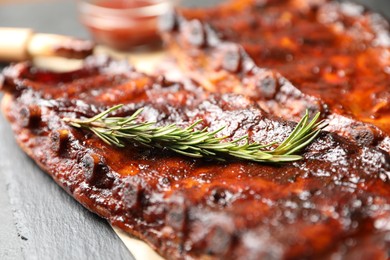 Photo of Tasty roasted pork ribs served with rosemary on black table, closeup