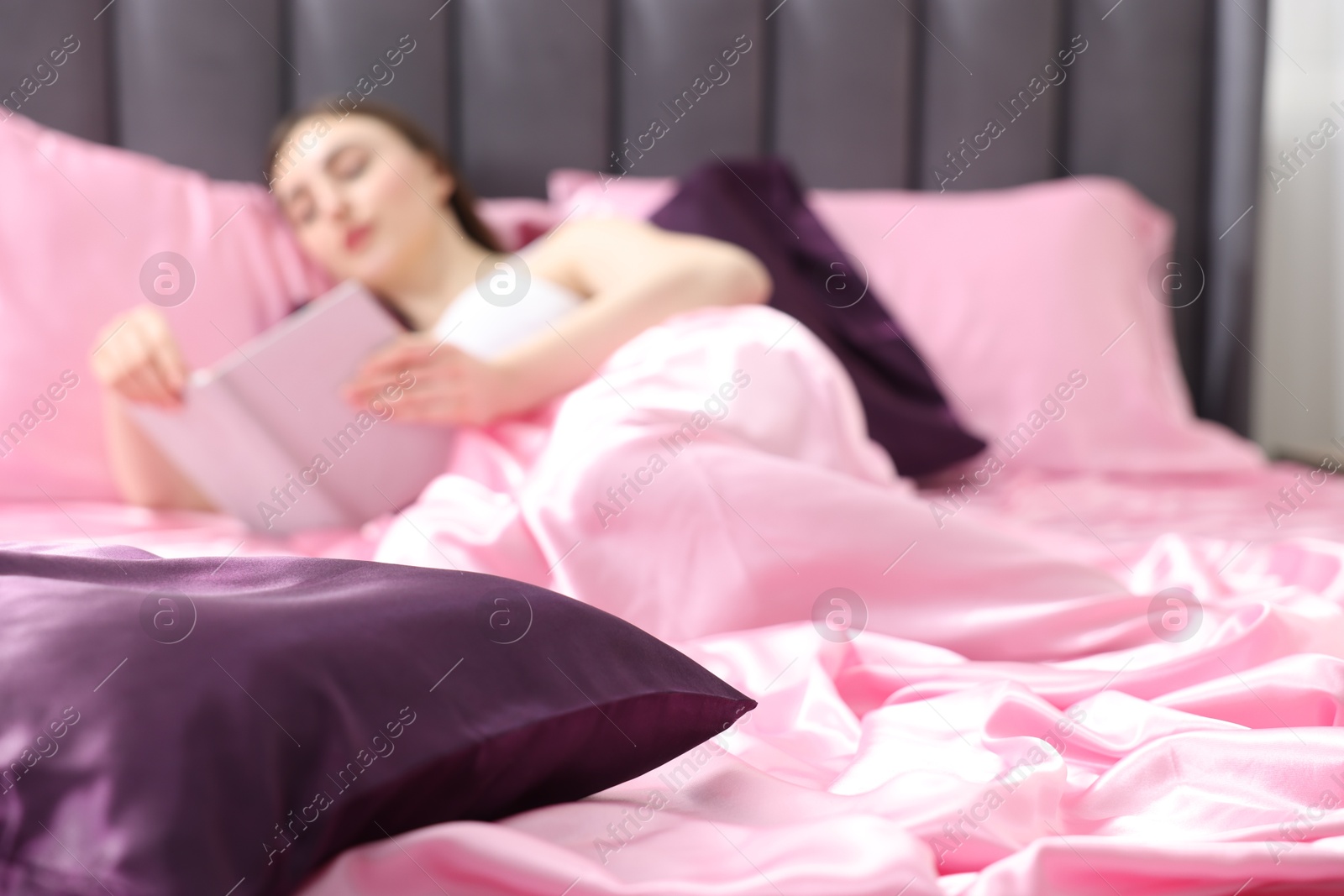 Woman reading book in bed with pink silk linens indoors, selective focus Photo of Woman reading book in bed with pink silk linens indoors, selective focus