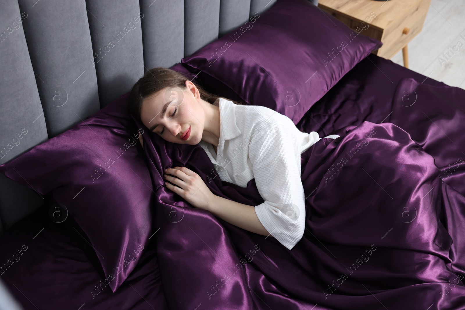 Woman sleeping in bed with purple silk linens indoors Photo of Woman sleeping in bed with purple silk linens indoors