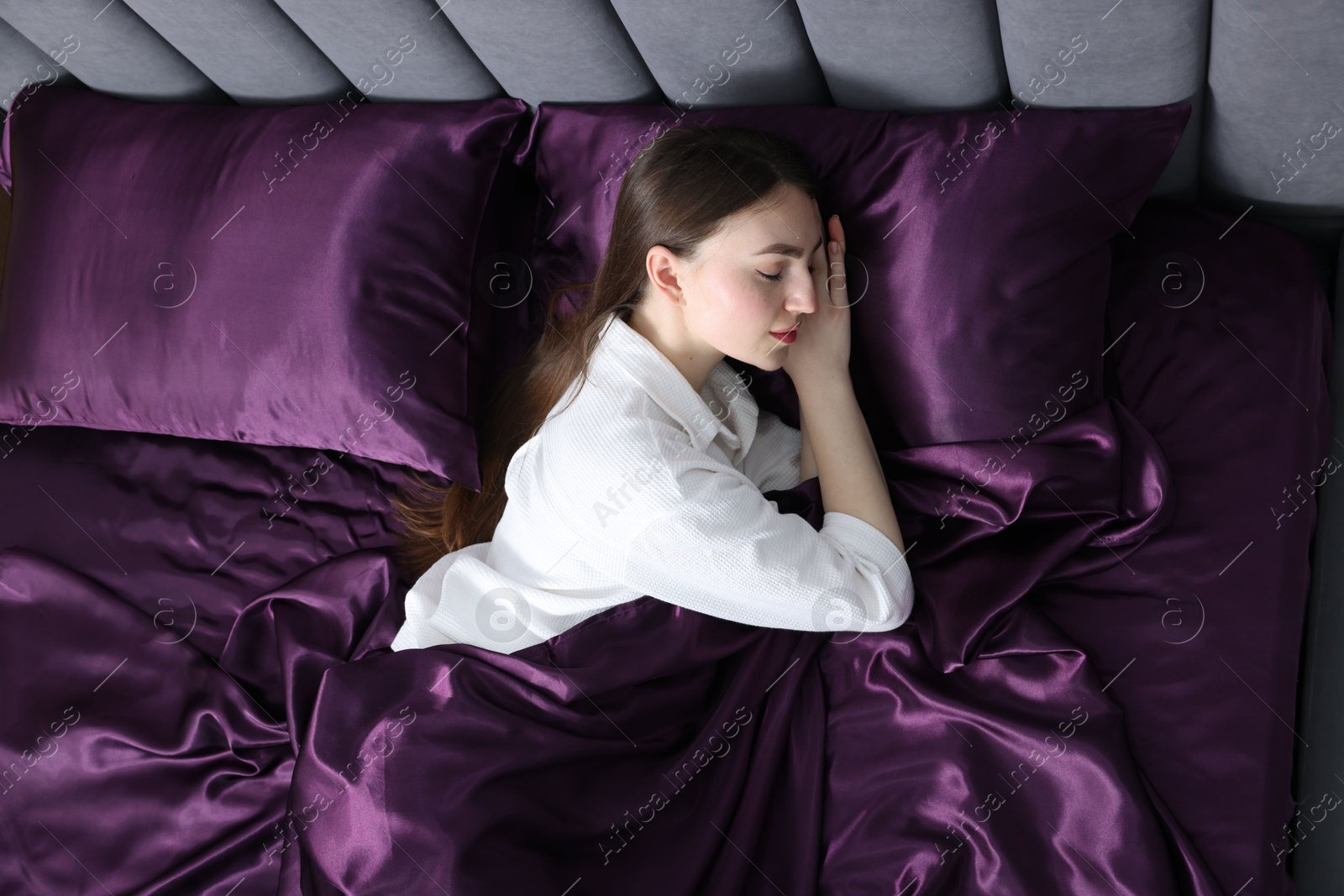 Woman sleeping in bed with purple silk linens, above view Photo of Woman sleeping in bed with purple silk linens, above view
