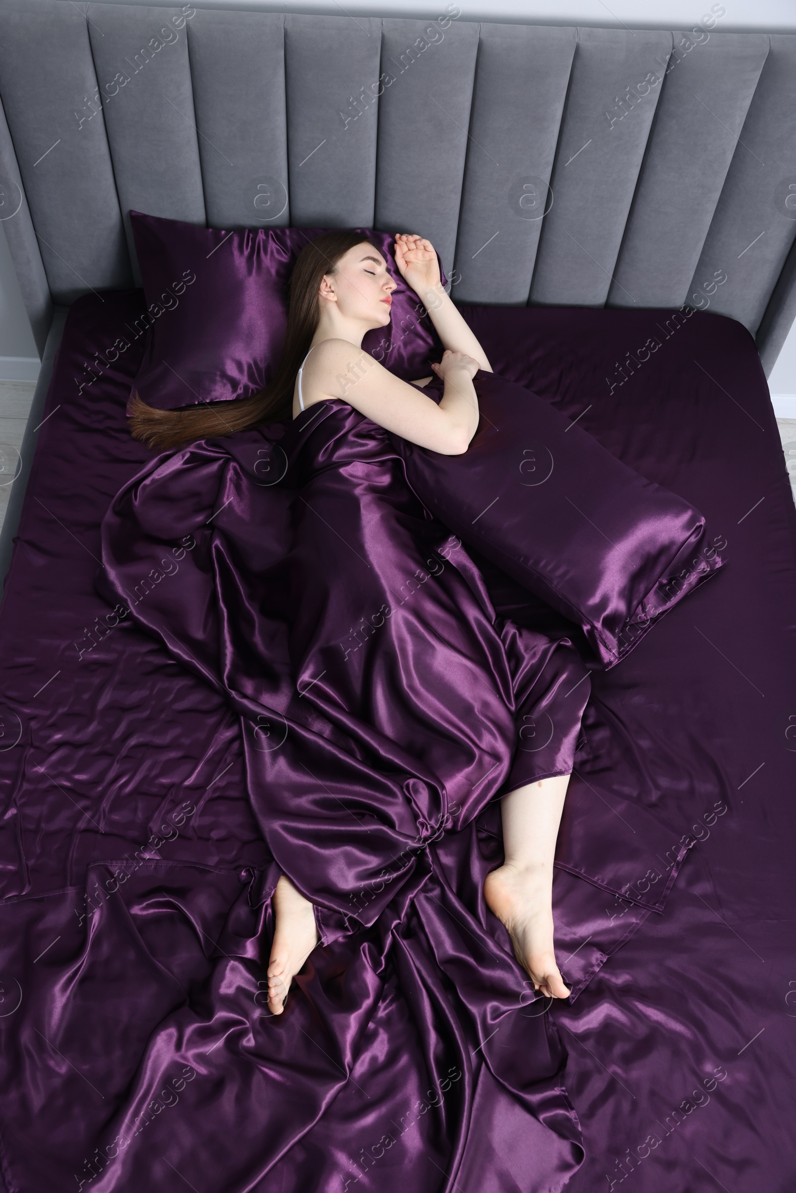 Woman sleeping in bed with purple silk linens indoors, above view Photo of Woman sleeping in bed with purple silk linens indoors, above view