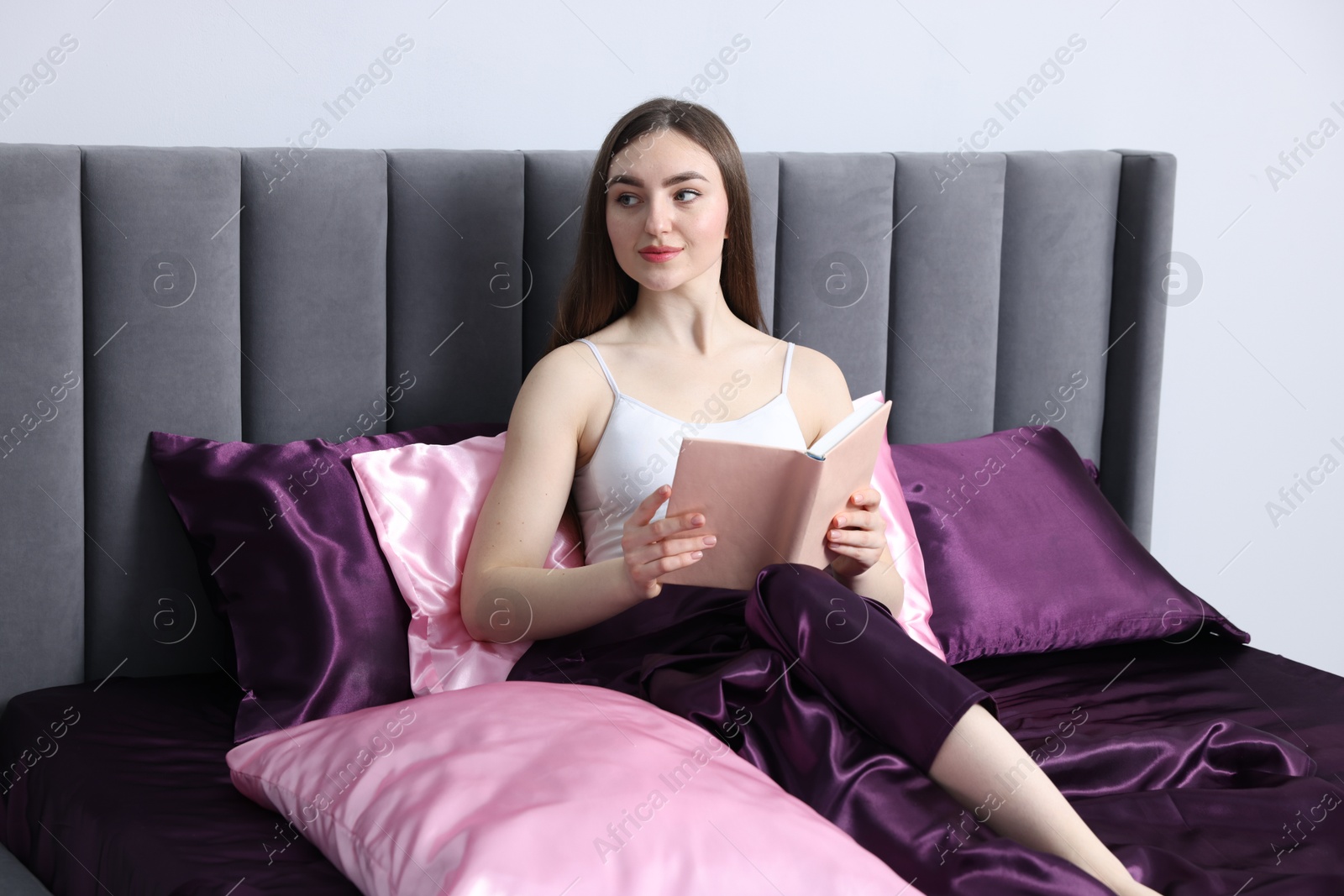Woman reading book in bed with silk linens indoors Photo of Woman reading book in bed with silk linens indoors