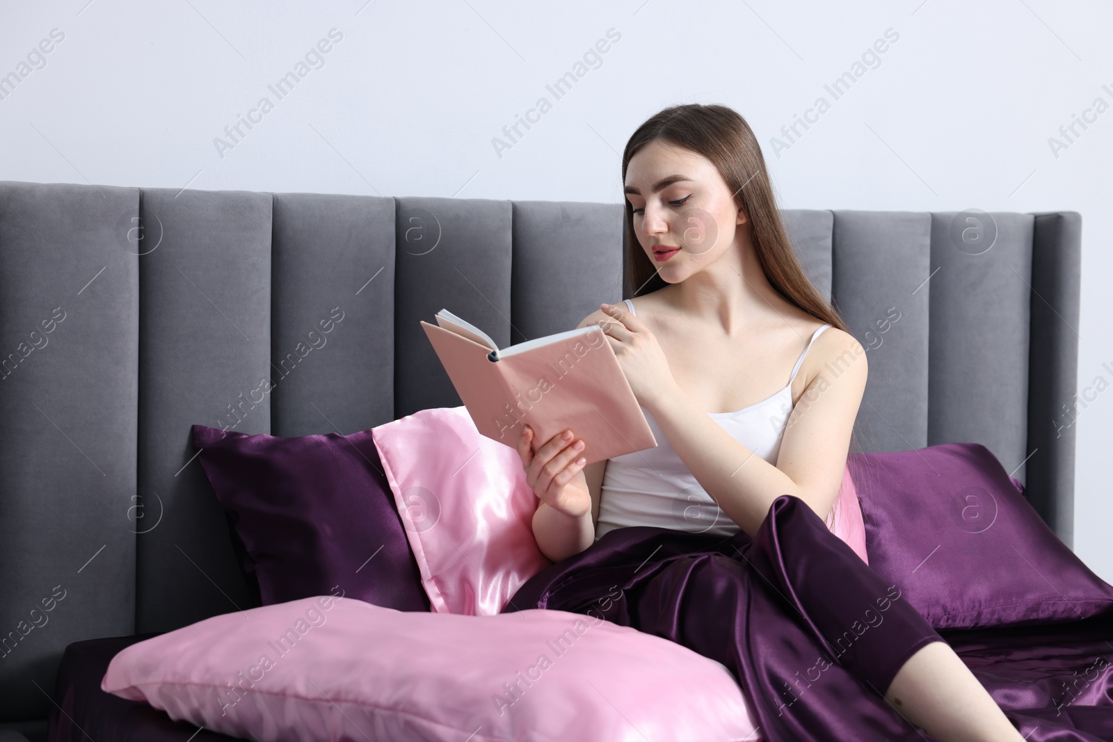 Woman reading book in bed with silk linens indoors Photo of Woman reading book in bed with silk linens indoors