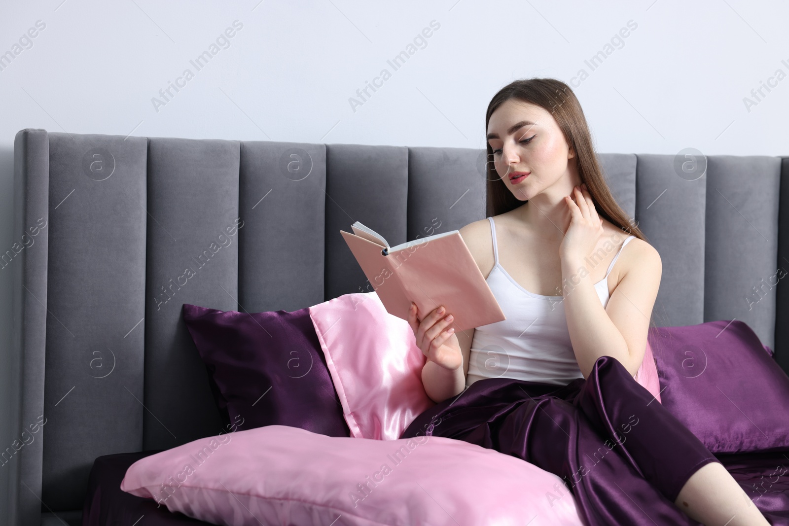Woman reading book in bed with silk linens indoors Photo of Woman reading book in bed with silk linens indoors