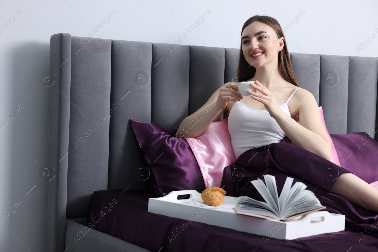 Smiling woman drinking coffee in bed with silk linens indoors Photo of Smiling woman drinking coffee in bed with silk linens indoors