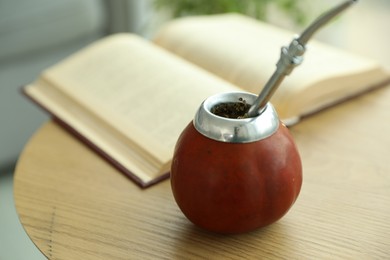 Photo of Traditional yerba mate tea and book on wooden table indoors, closeup