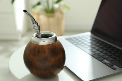 Photo of Traditional yerba mate tea and laptop on white table, closeup