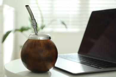 Photo of Traditional yerba mate tea and laptop on white table, closeup