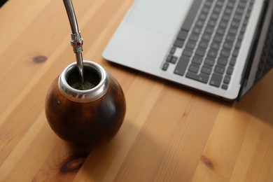 Photo of Traditional yerba mate tea and laptop on wooden table, closeup