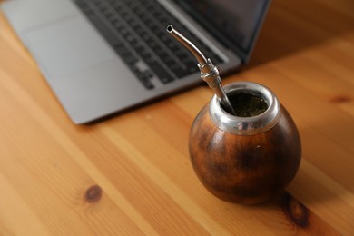 Photo of Traditional yerba mate tea and laptop on wooden table, closeup