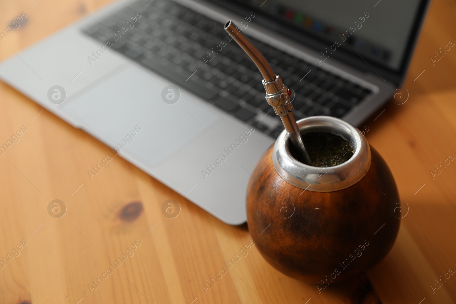 Traditional yerba mate tea and laptop on wooden table, closeup Photo of Traditional yerba mate tea and laptop on wooden table, closeup