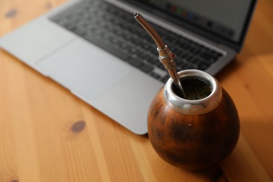 Photo of Traditional yerba mate tea and laptop on wooden table, closeup