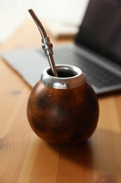 Photo of Traditional yerba mate tea and laptop on wooden table, closeup