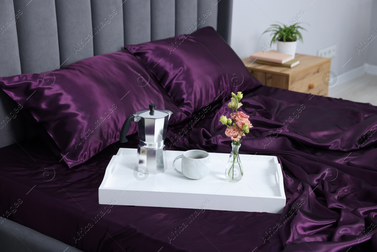 Purple silk linens, tray with coffee and flowers on bed indoors Photo of Purple silk linens, tray with coffee and flowers on bed indoors
