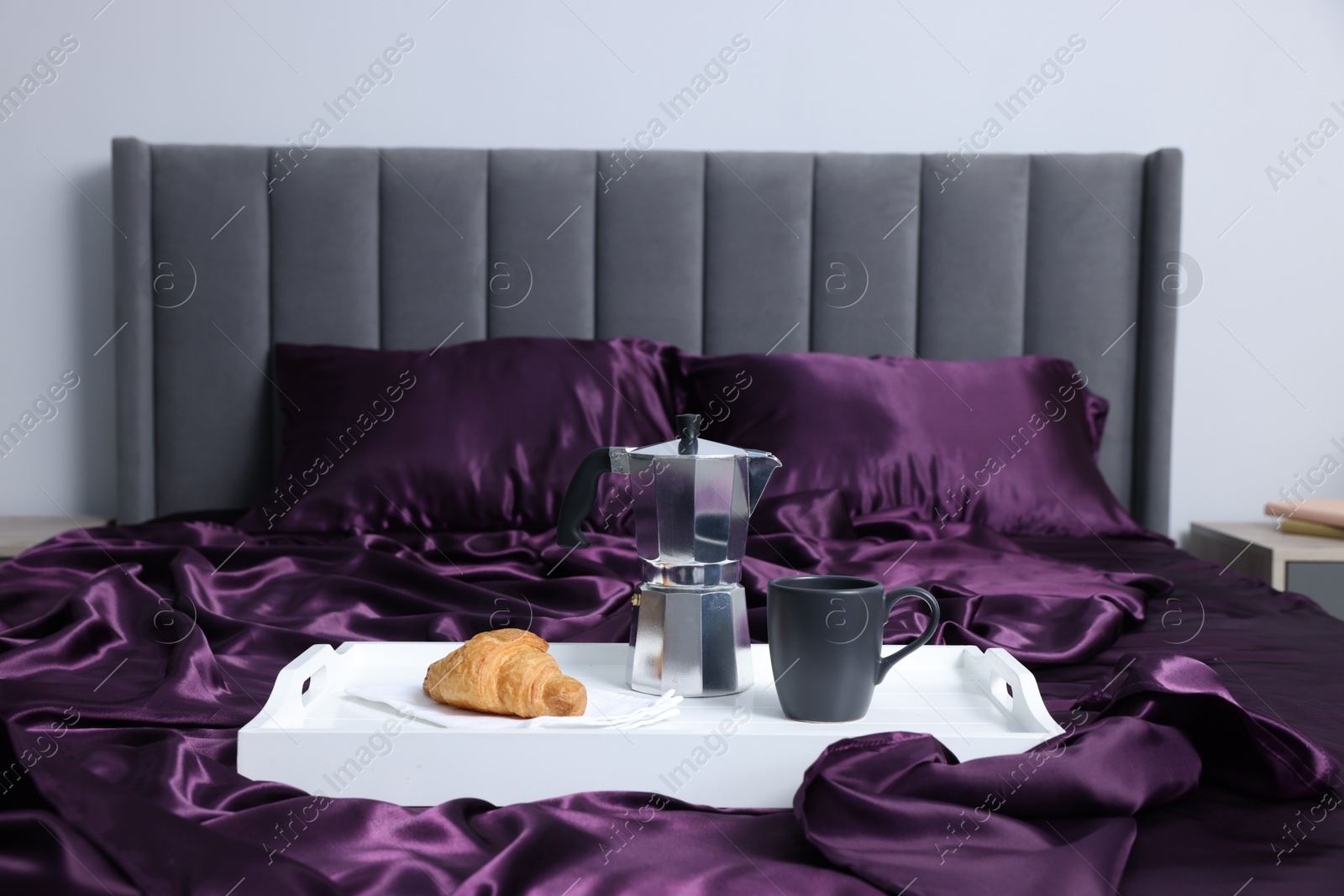 Purple silk linens, tray with coffee and croissant on bed indoors Photo of Purple silk linens, tray with coffee and croissant on bed indoors