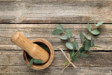 Photo of Beautiful eucalyptus branches, mortar and pestle on wooden background, top view