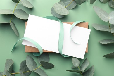 Photo of Blank card, ribbon and eucalyptus branches on light green background, flat lay