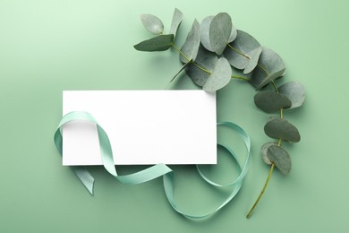 Photo of Blank card, ribbon and eucalyptus branches on light green background, flat lay