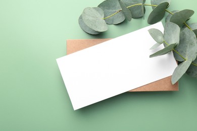 Photo of Blank card and eucalyptus branches on light green background, flat lay