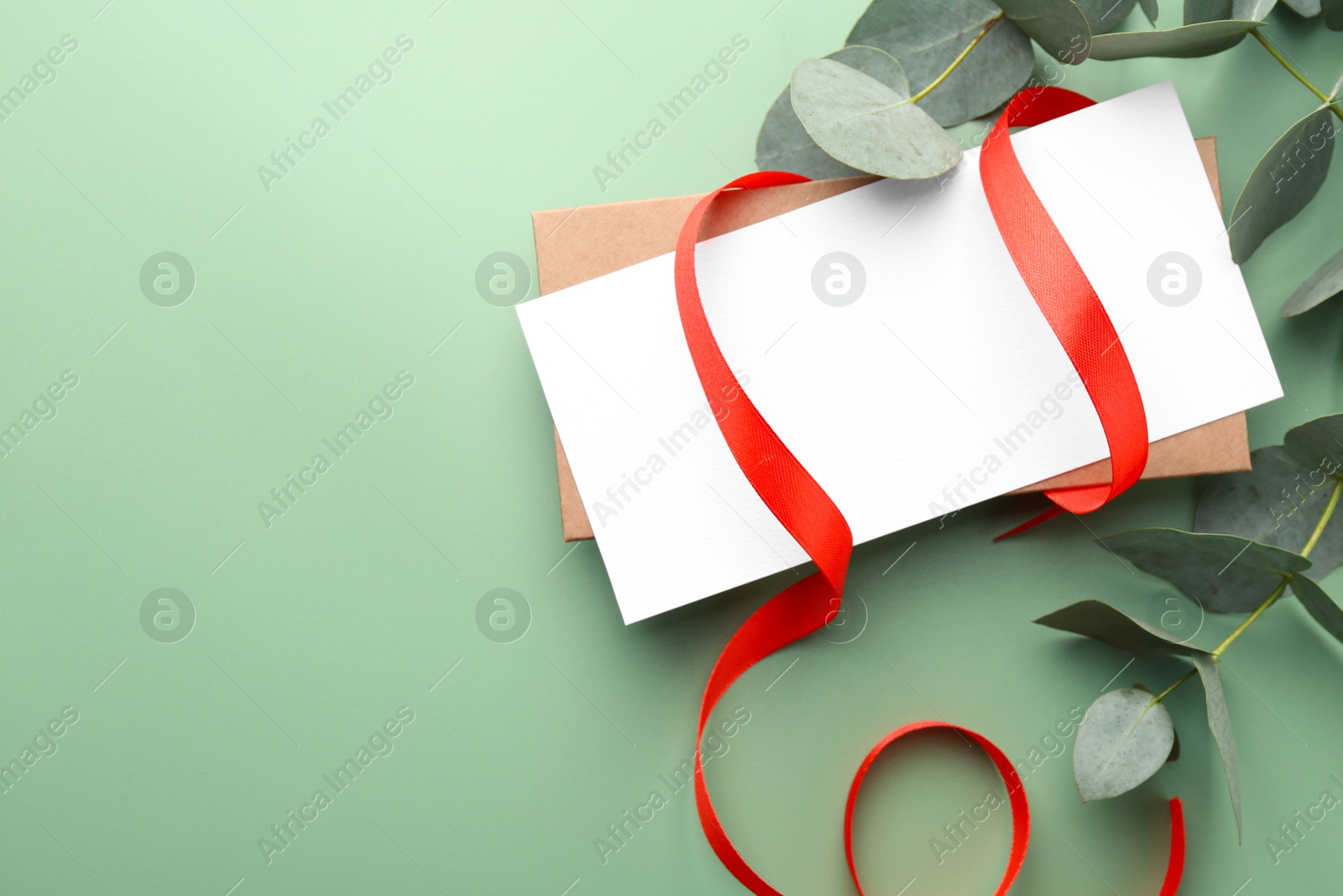 Blank card, ribbon and eucalyptus branches on light green background, flat lay. Space for text Photo of Blank card, ribbon and eucalyptus branches on light green background, flat lay. Space for text