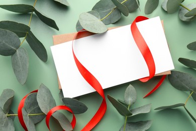 Photo of Blank card, ribbon and eucalyptus branches on light green background, flat lay