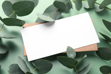 Photo of Blank card and eucalyptus branches on light green background, closeup