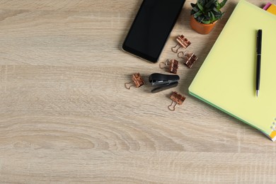 Photo of Flat lay composition with office supplies, smartphone and houseplant on wooden table. Space for text