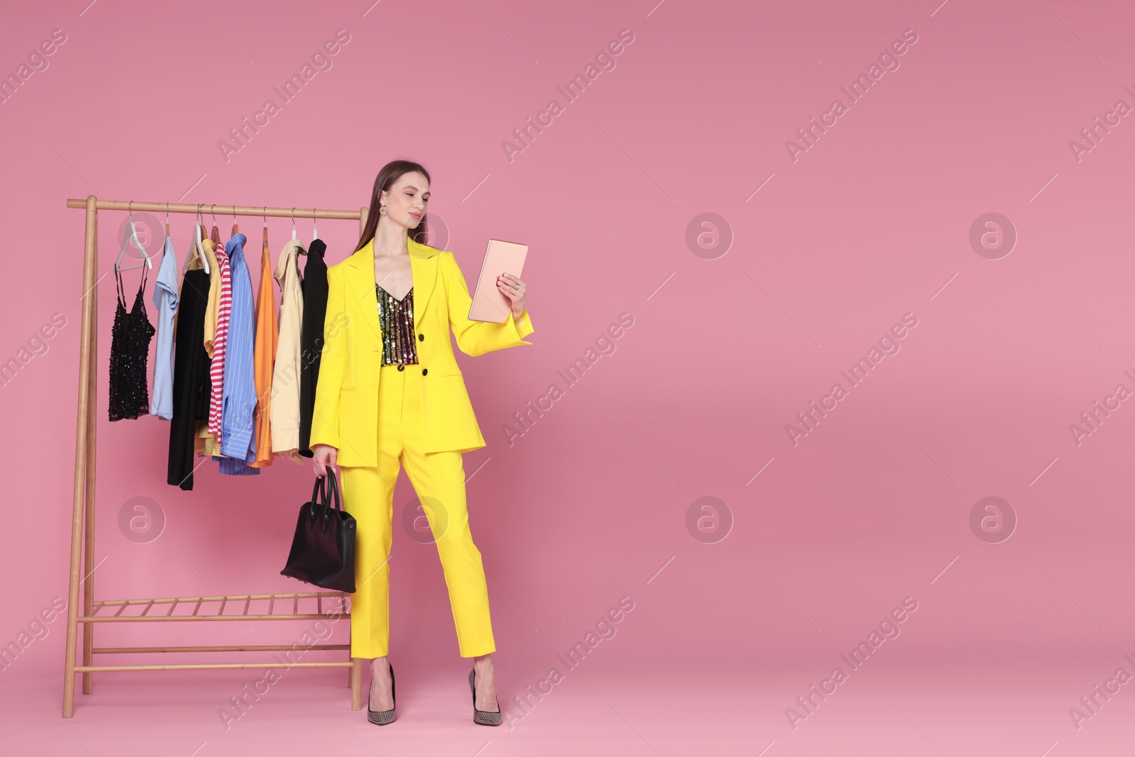 Fashion stylist with tablet, bag and clothing rack on pink background. Space for text Photo of Fashion stylist with tablet, bag and clothing rack on pink background. Space for text