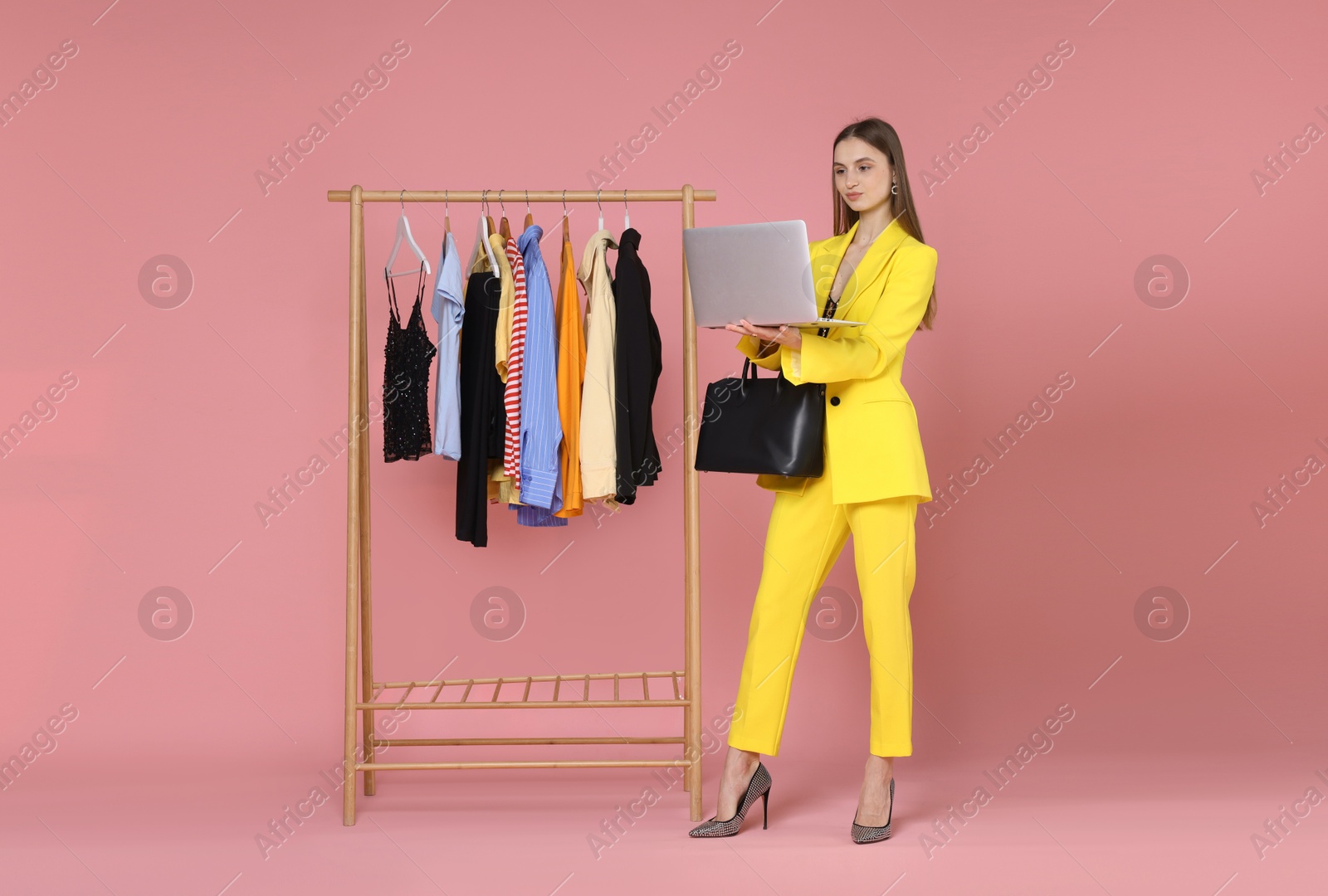 Fashion stylist with laptop, bag and clothing rack on pink background Photo of Fashion stylist with laptop, bag and clothing rack on pink background