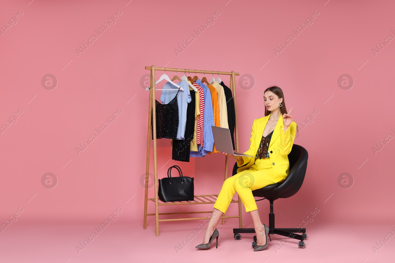 Fashion stylist with laptop and clothing rack on pink background. Space for text Photo of Fashion stylist with laptop and clothing rack on pink background. Space for text
