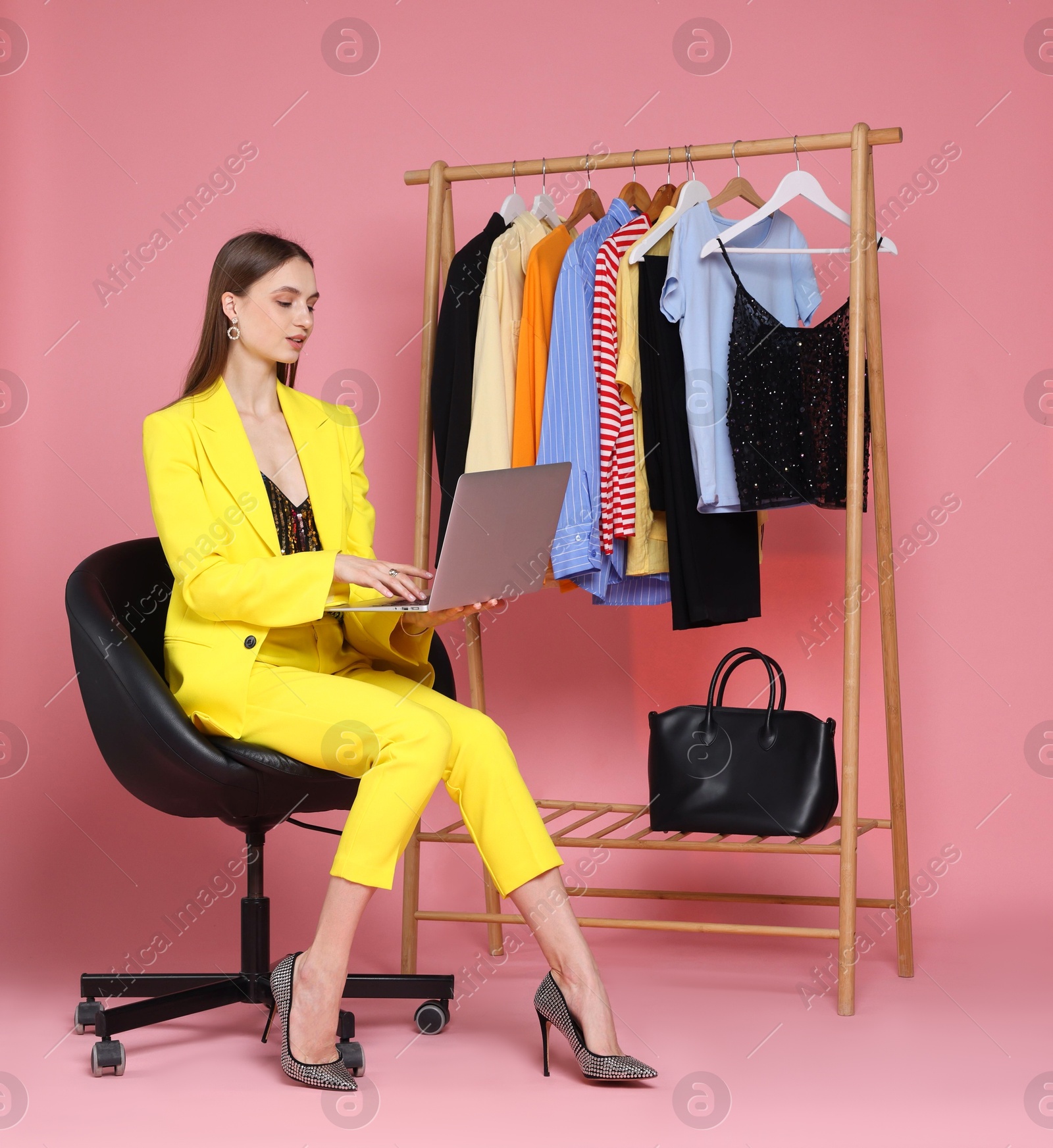 Fashion stylist working with laptop and clothing rack on pink background Photo of Fashion stylist working with laptop and clothing rack on pink background