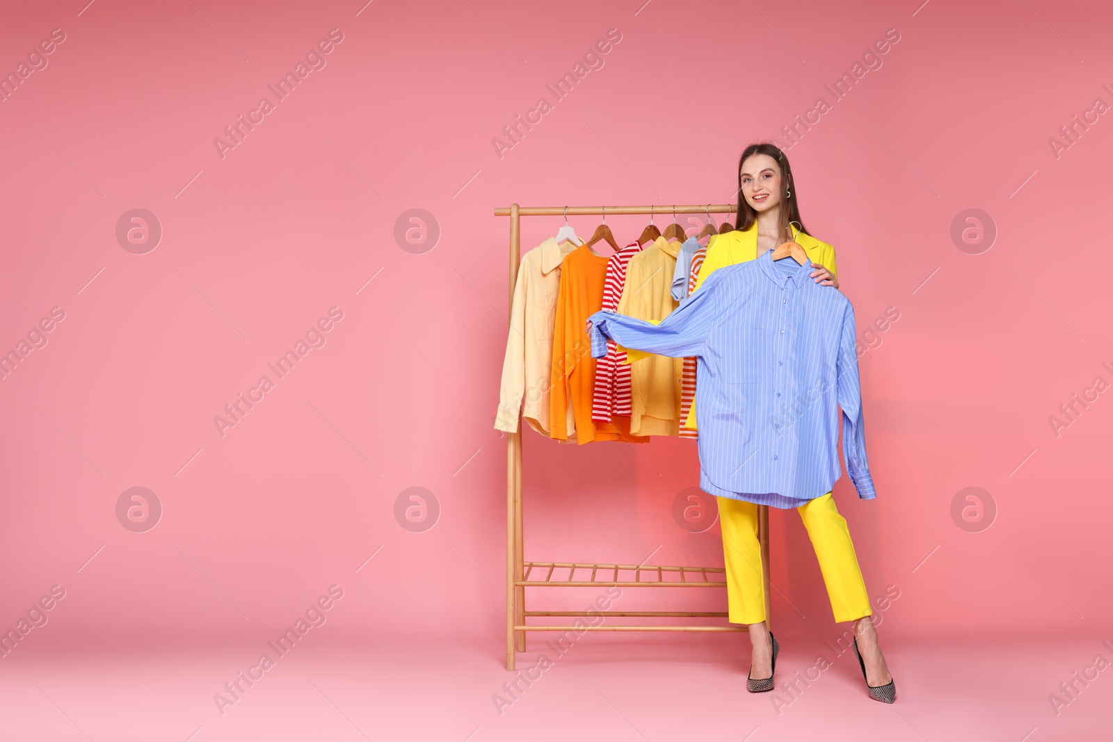 Smiling fashion stylist with shirt and clothing rack on pink background. Space for text Photo of Smiling fashion stylist with shirt and clothing rack on pink background. Space for text