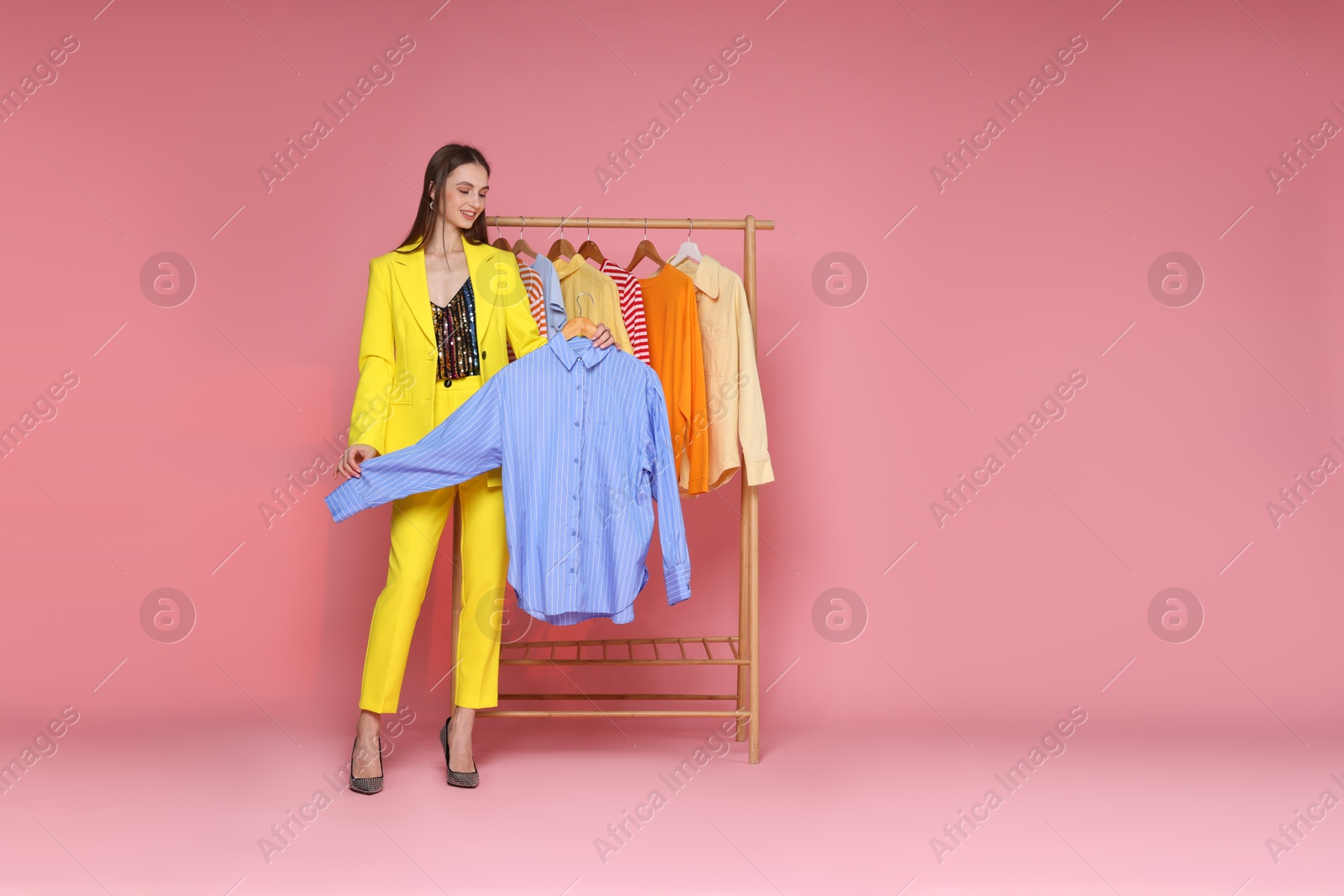 Smiling fashion stylist with shirt and clothing rack on pink background. Space for text Photo of Smiling fashion stylist with shirt and clothing rack on pink background. Space for text