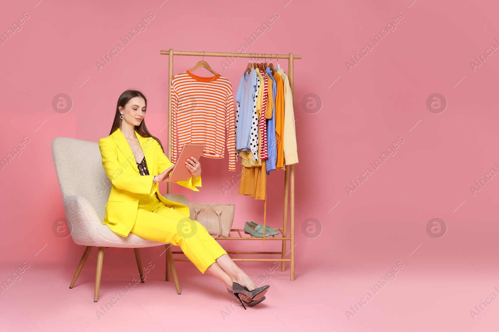 Fashion stylist working with tablet and clothing rack on pink background. Space for text Photo of Fashion stylist working with tablet and clothing rack on pink background. Space for text